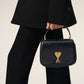 Black handbag with a gold heart and arrow design on a beige background