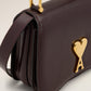 Burgundy handbag with a gold heart and letter 'A' emblem on a beige background