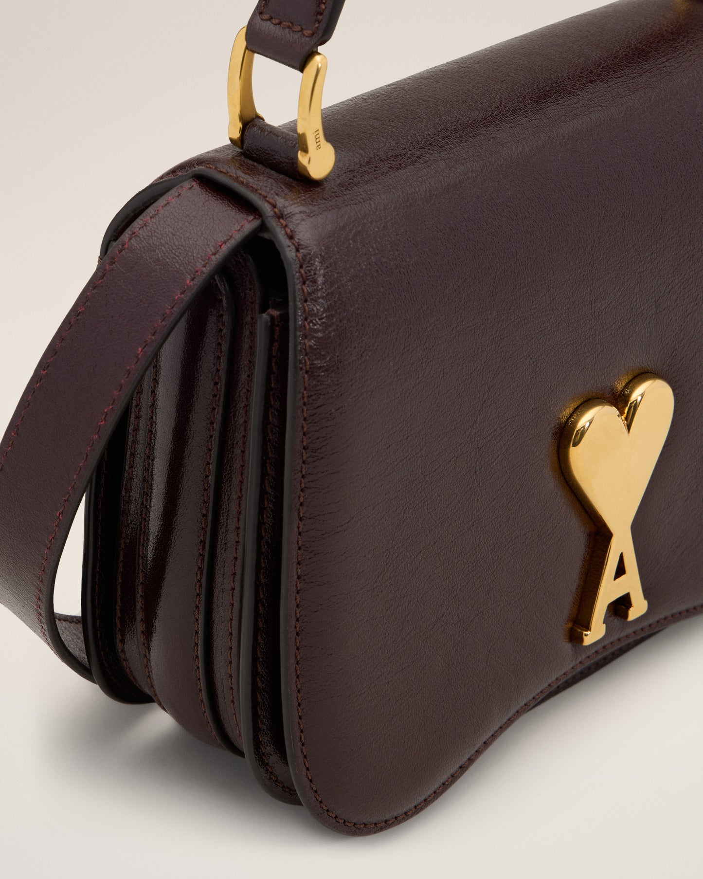 Burgundy handbag with a gold heart and letter 'A' emblem on a beige background