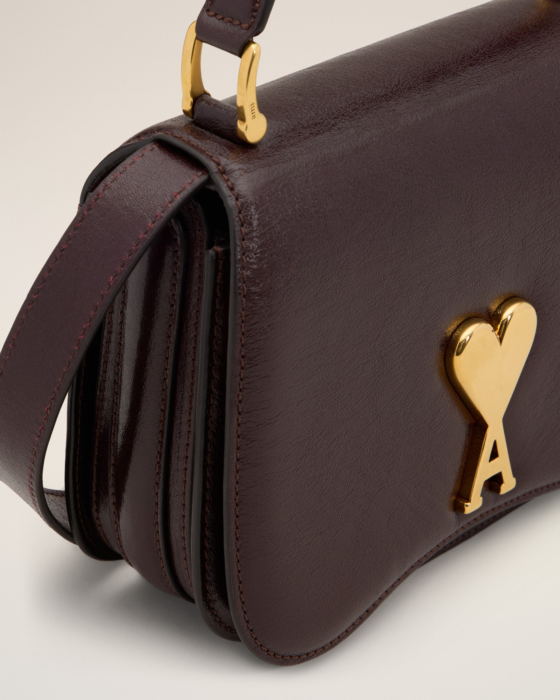 Burgundy handbag with a gold heart and letter 'A' emblem on a beige background