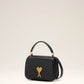 Black handbag with a gold heart and arrow design on a beige background