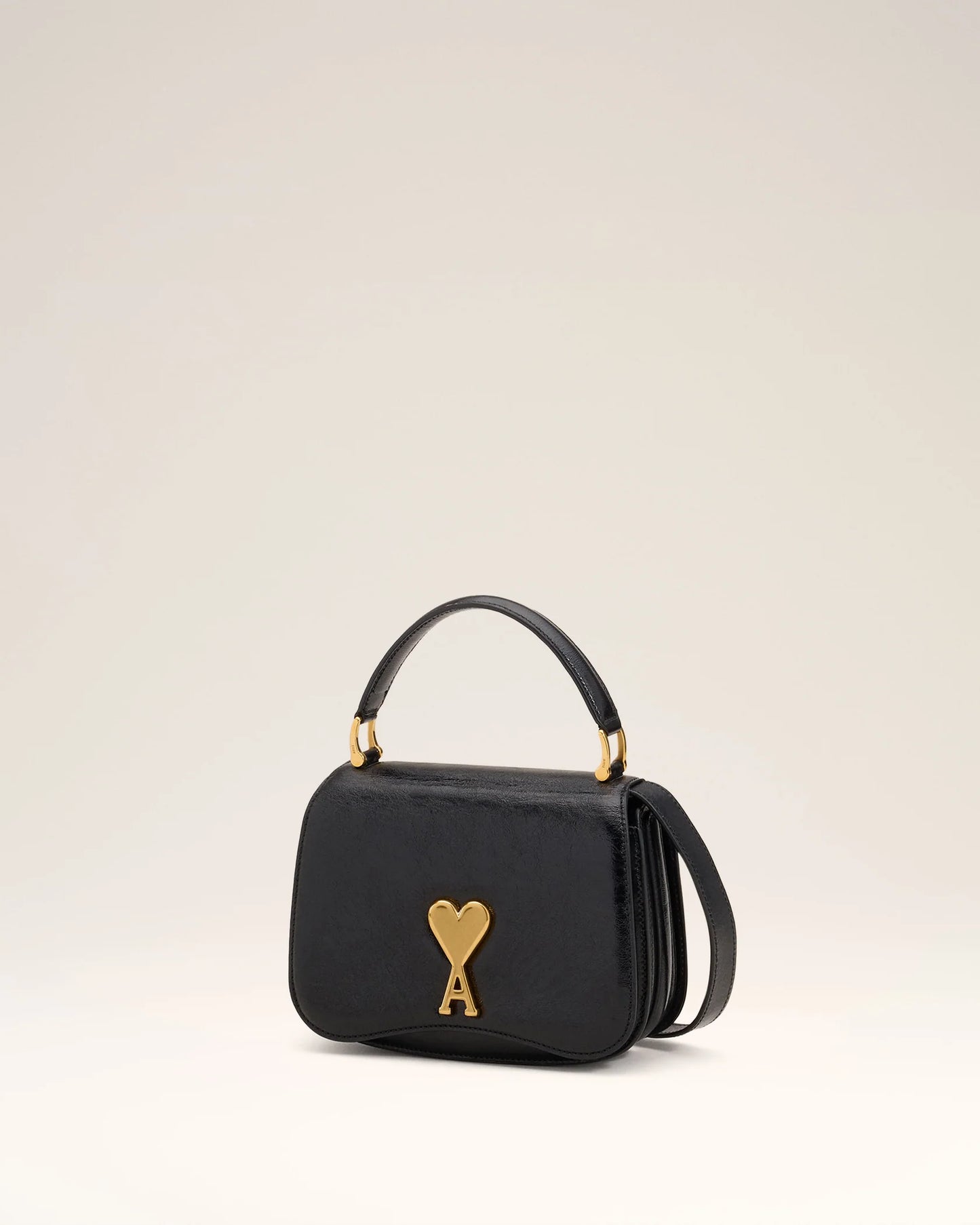 Black handbag with a gold heart and arrow design on a beige background