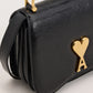 Black handbag with a gold heart and arrow design on a beige background