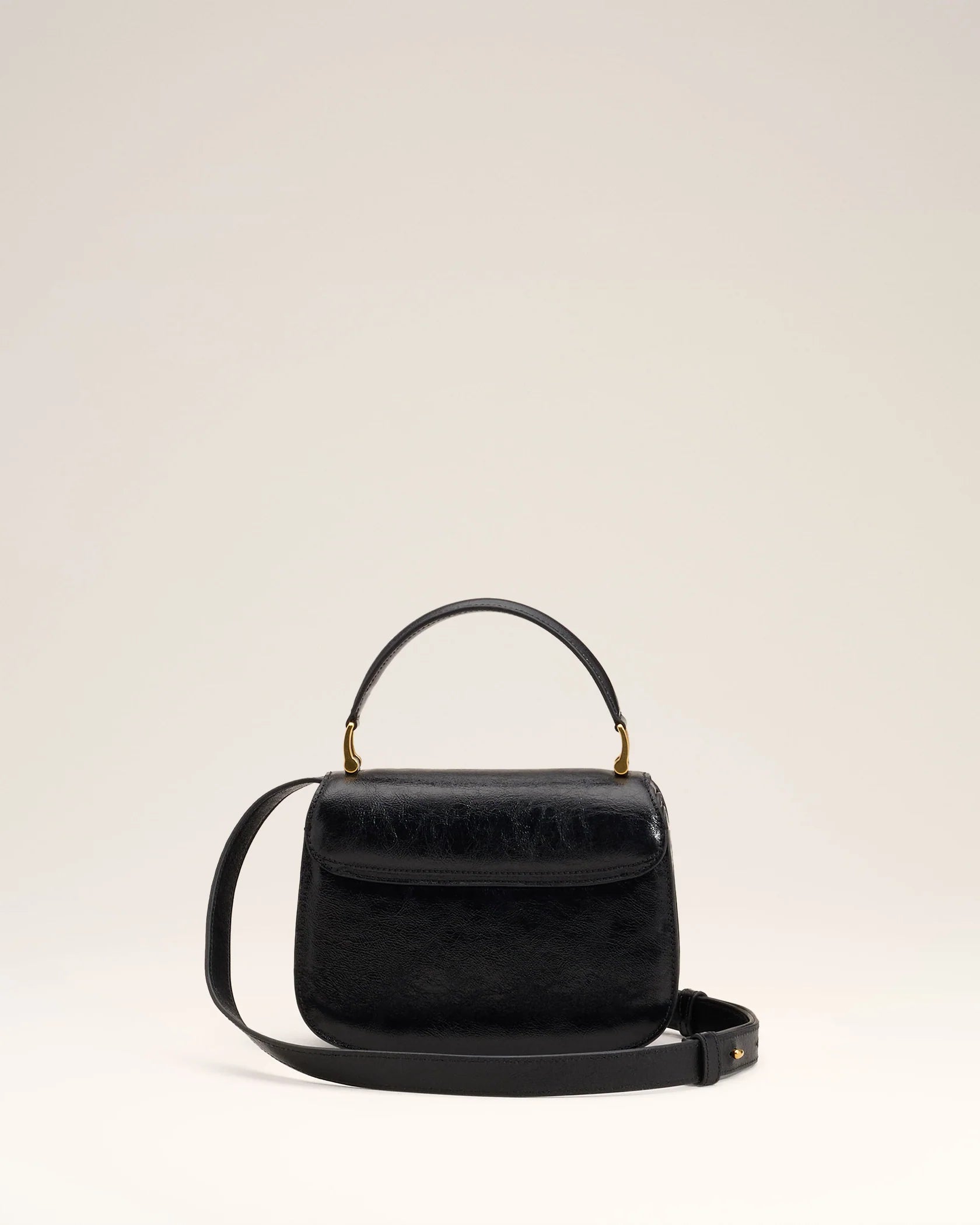 Black handbag with a gold heart and arrow design on a beige background