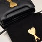 Black handbag with a gold heart and arrow design on a beige background