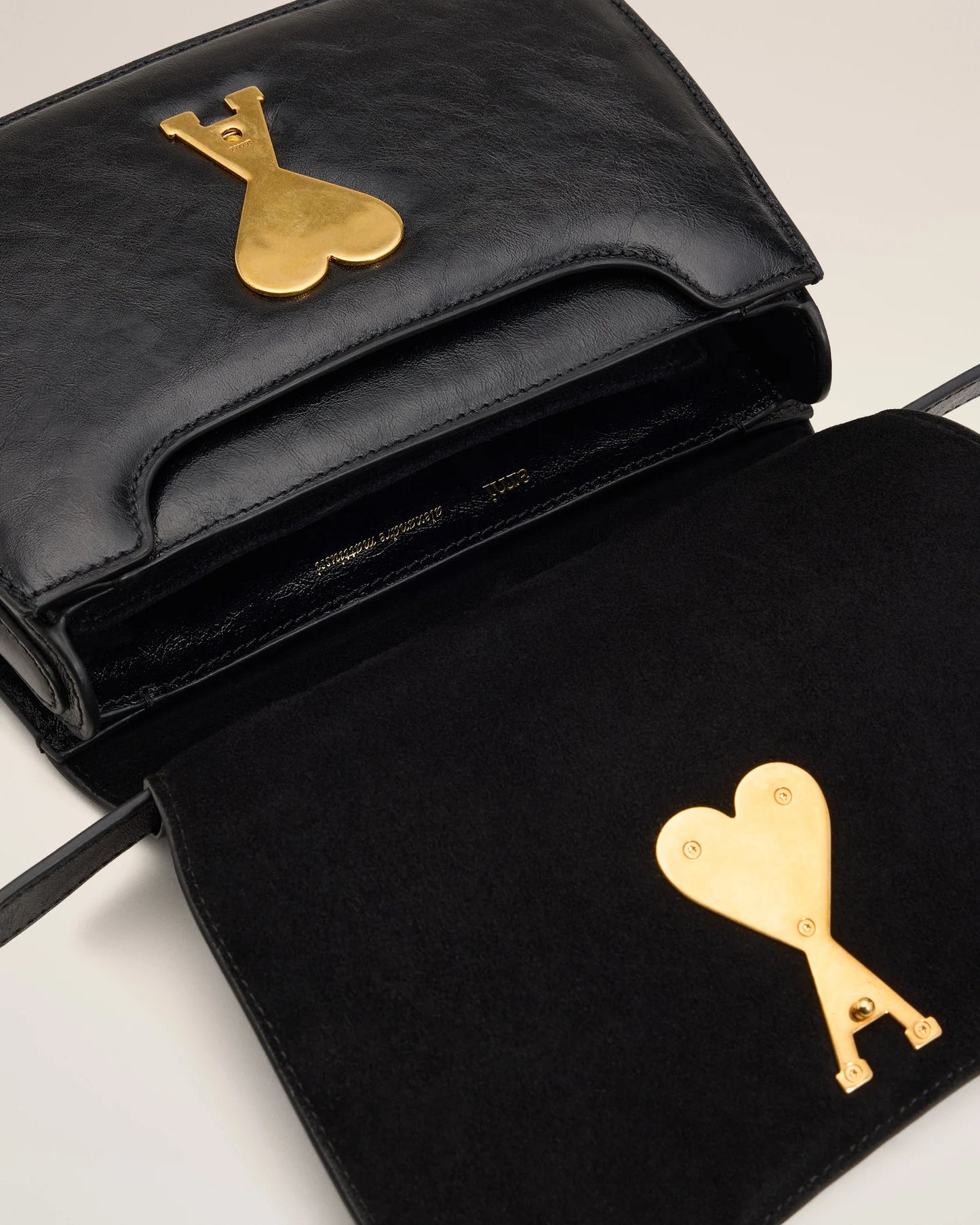 Black handbag with a gold heart and arrow design on a beige background