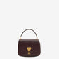 Burgundy handbag with a gold heart and letter 'A' emblem on a beige background
