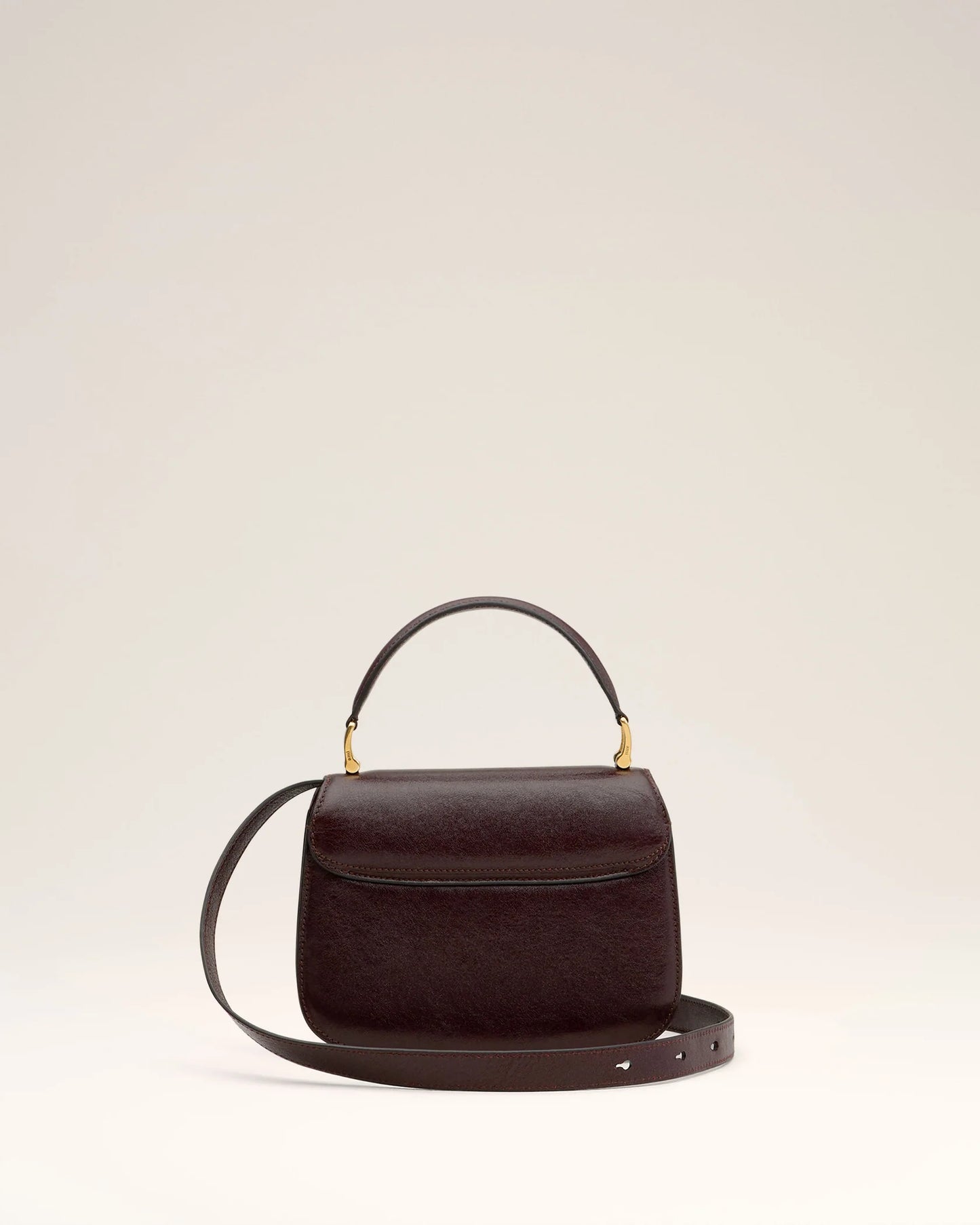 Burgundy handbag with a gold heart and letter 'A' emblem on a beige background