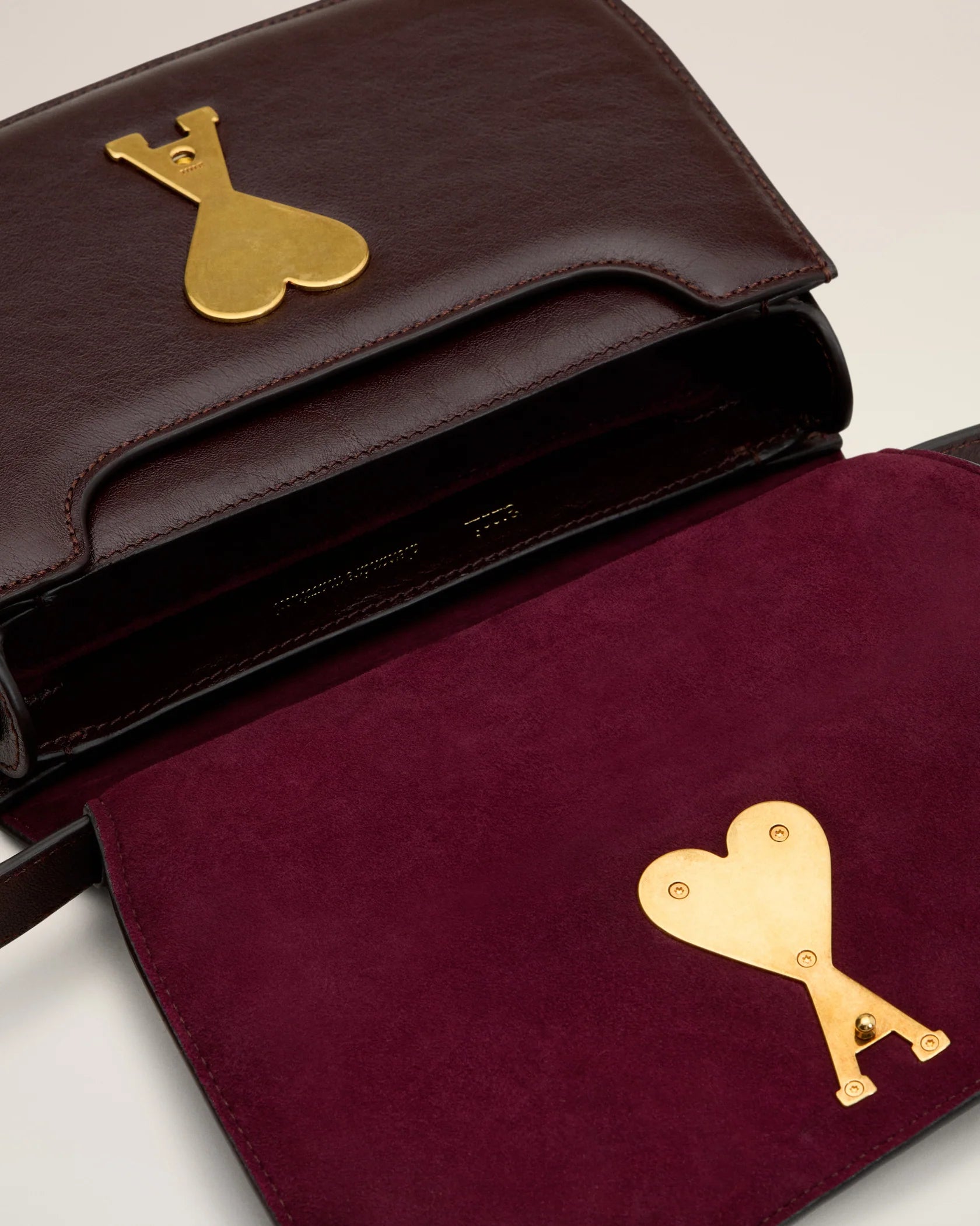Burgundy handbag with a gold heart and letter 'A' emblem on a beige background
