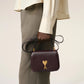 Burgundy handbag with a gold heart and letter 'A' emblem on a beige background