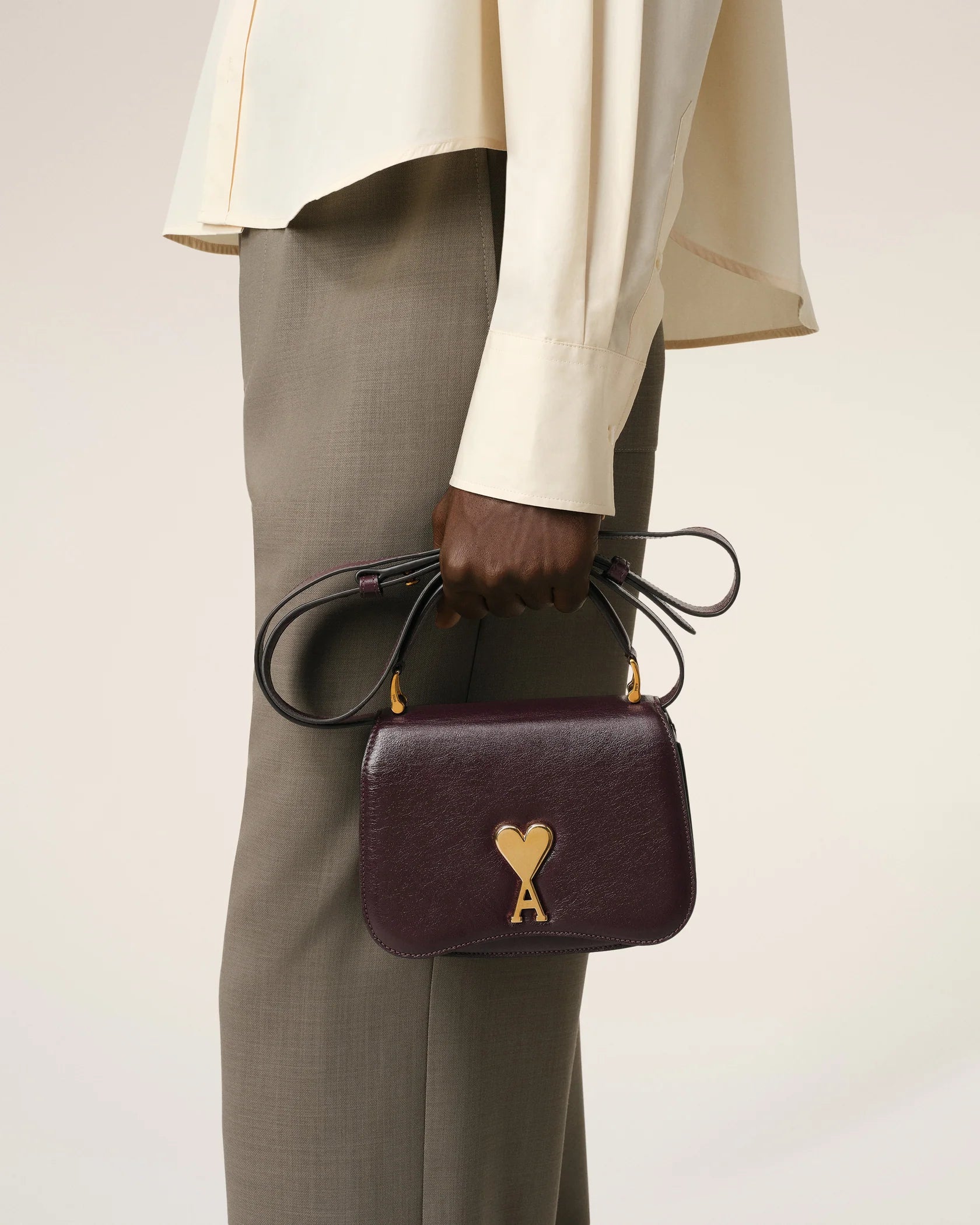 Burgundy handbag with a gold heart and letter 'A' emblem on a beige background