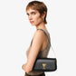 Woman carrying a black handbag with a gold heart emblem on a plain background