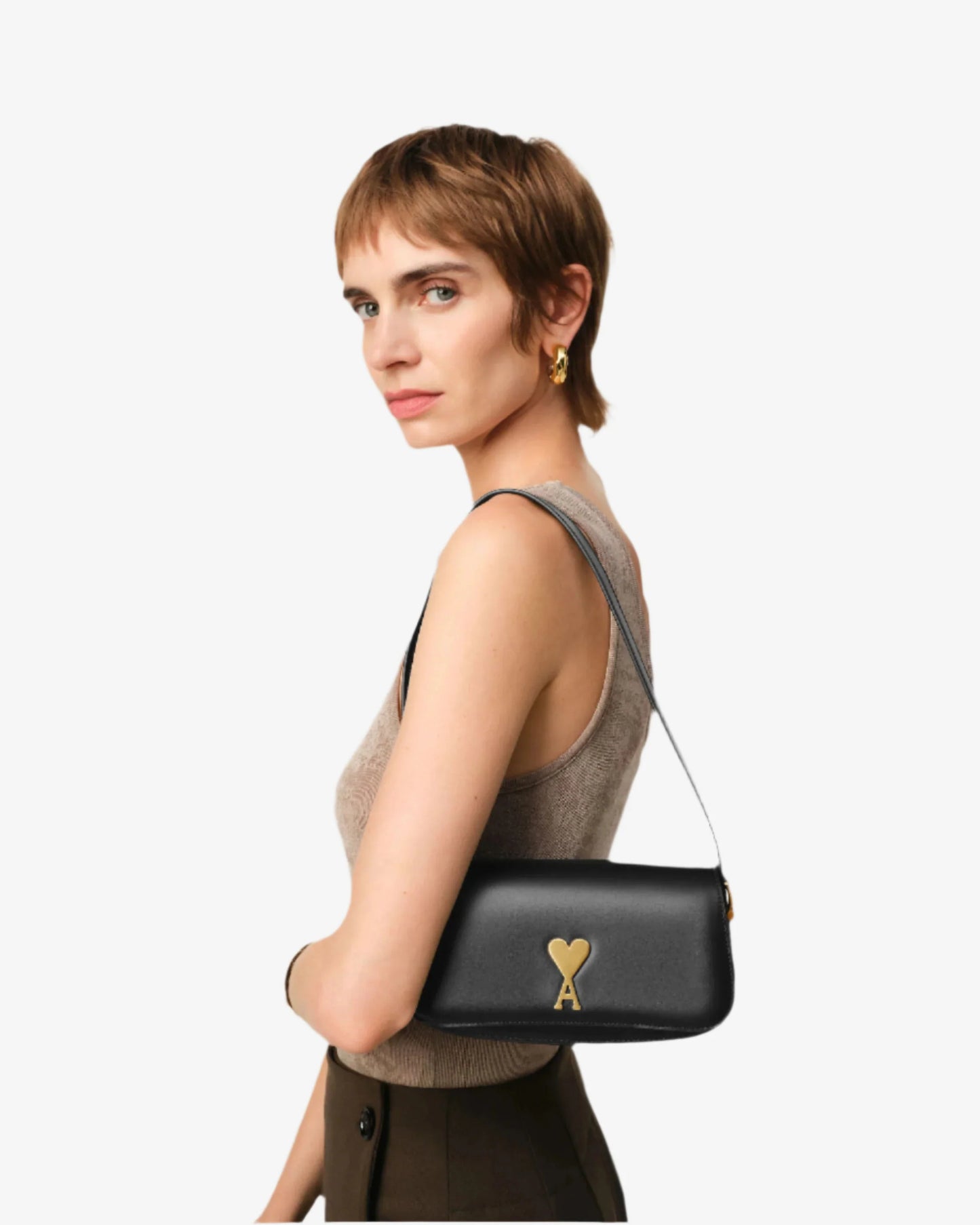 Woman carrying a black handbag with a gold heart emblem on a plain background