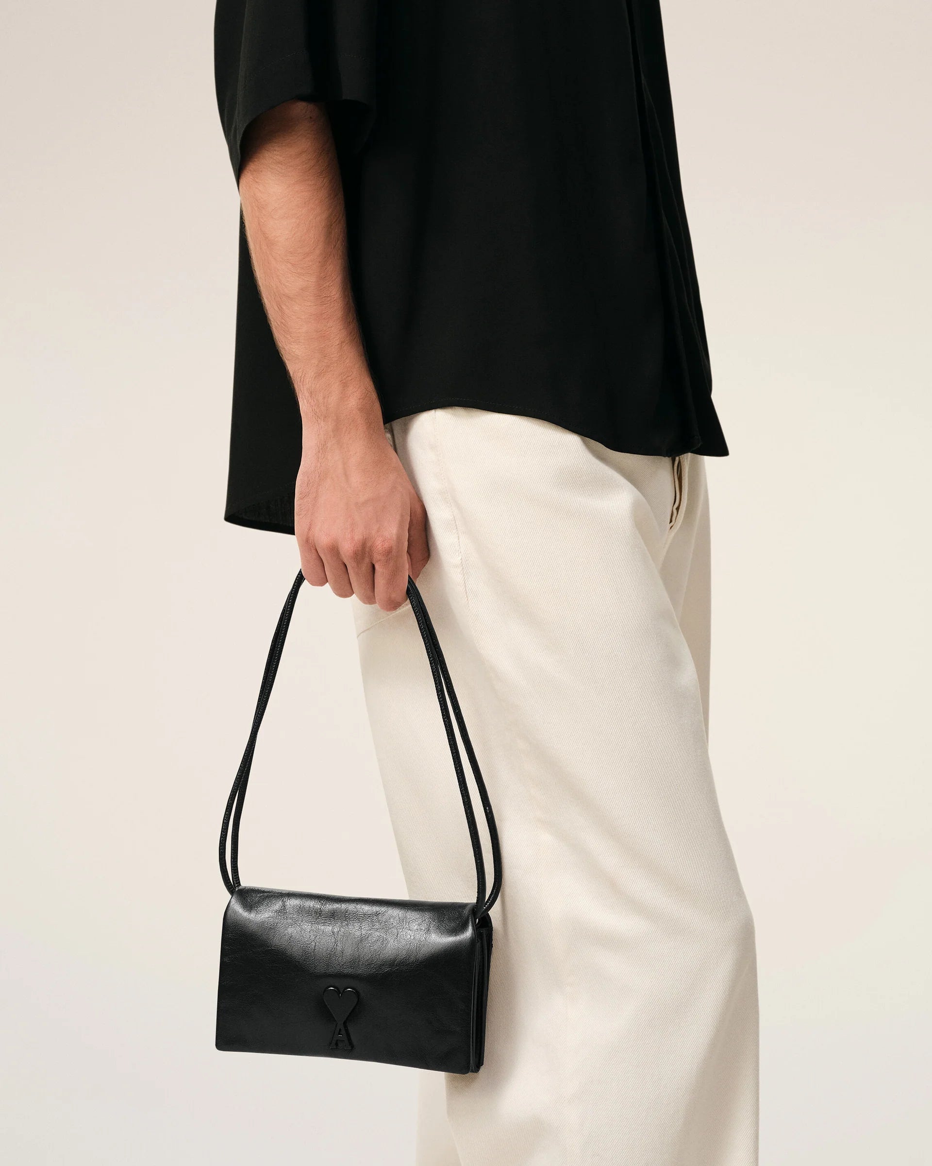 Person holding a black handbag against a neutral background