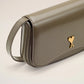 Green handbag with a gold heart emblem on a light beige background ami paris