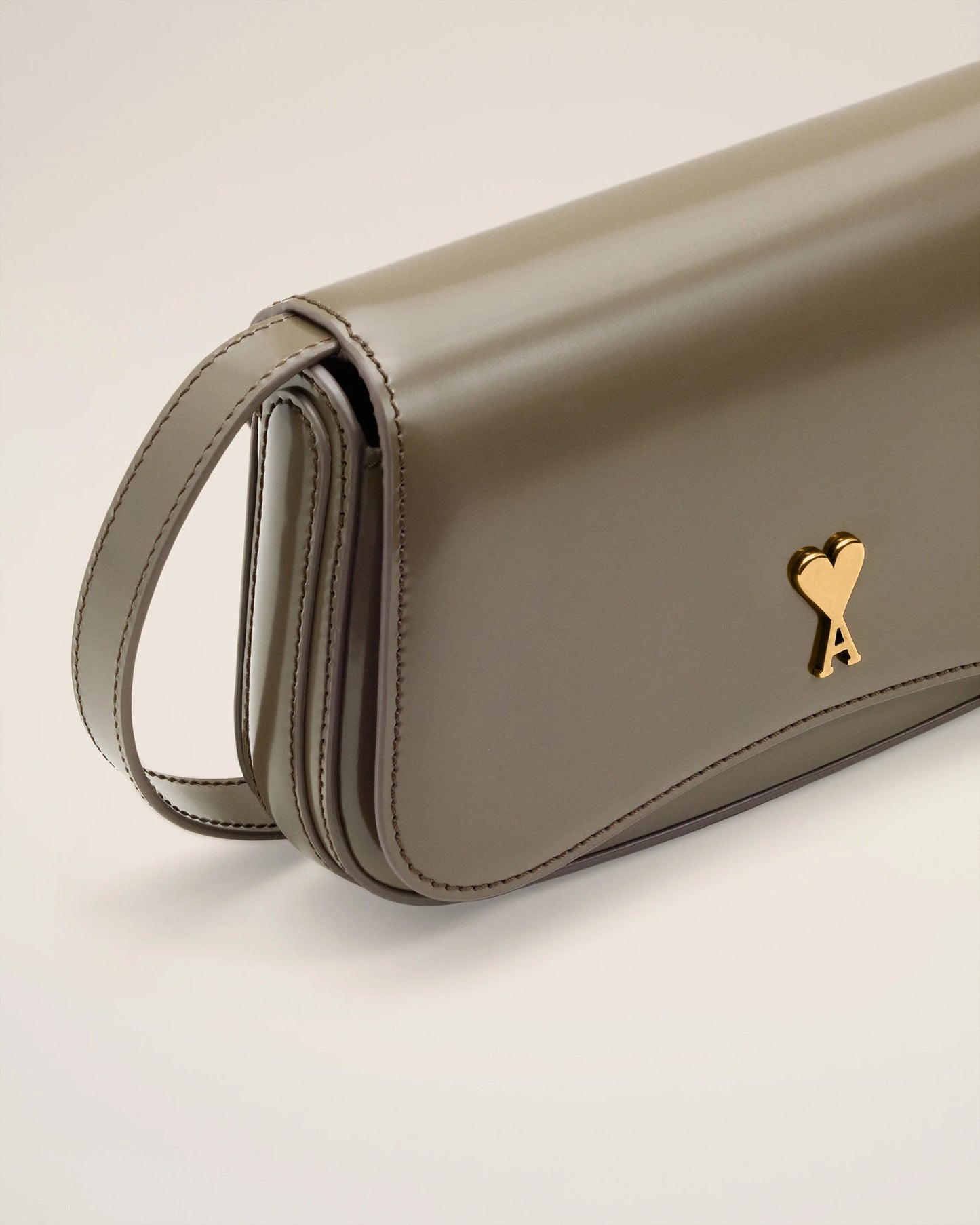 Green handbag with a gold heart emblem on a light beige background ami paris