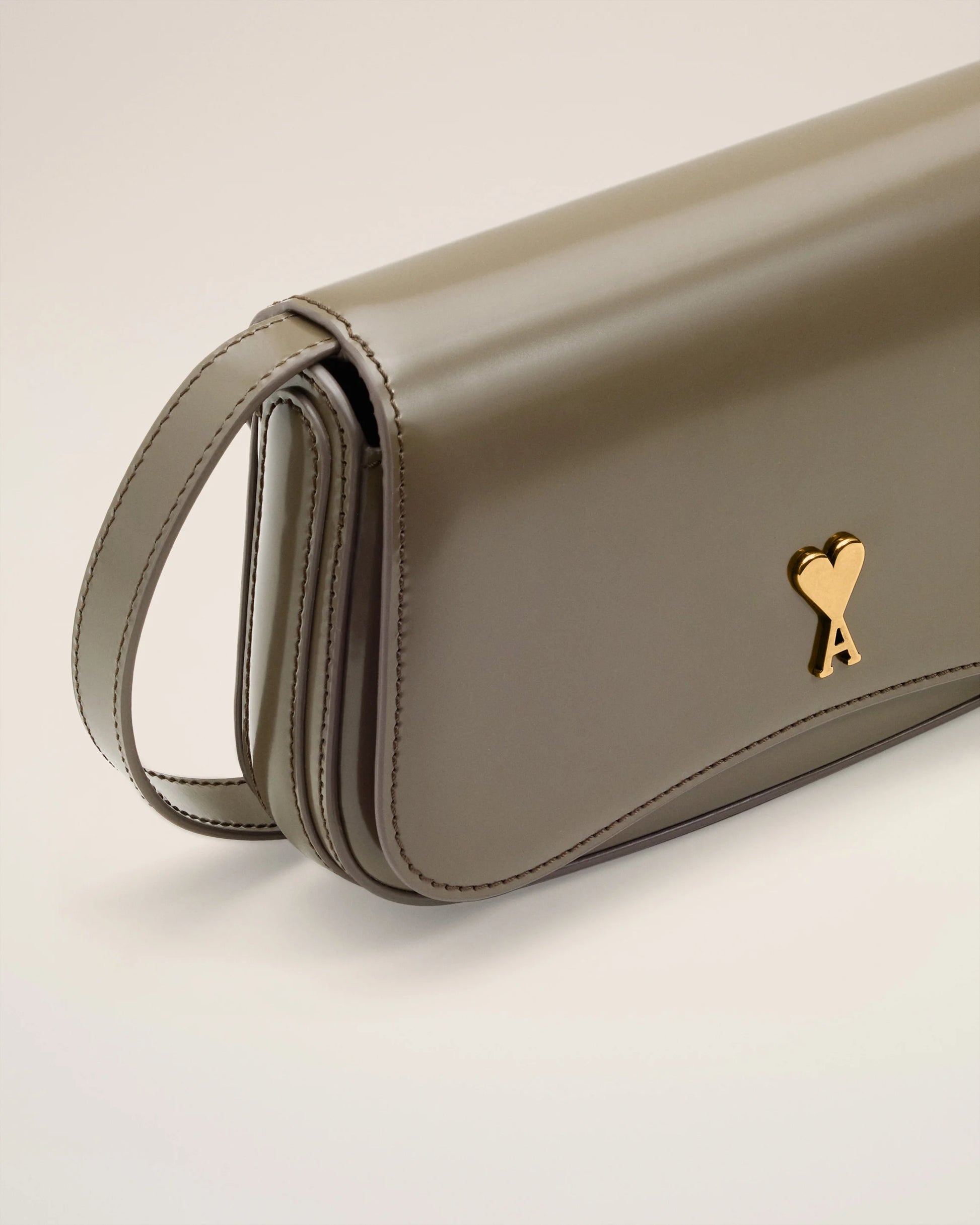 Green handbag with a gold heart emblem on a light beige background ami paris