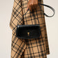 Person holding a black handbag with a gold emblem against a neutral background ami paris