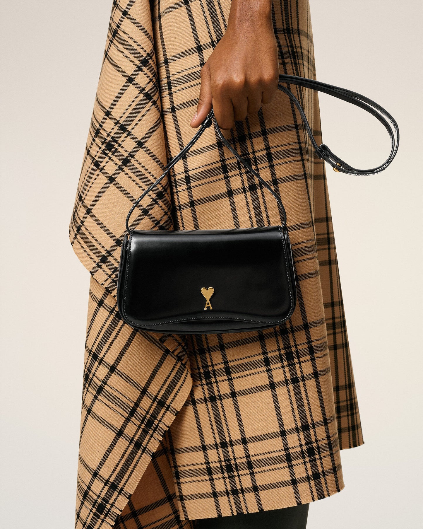 Person holding a black handbag with a gold emblem against a neutral background ami paris