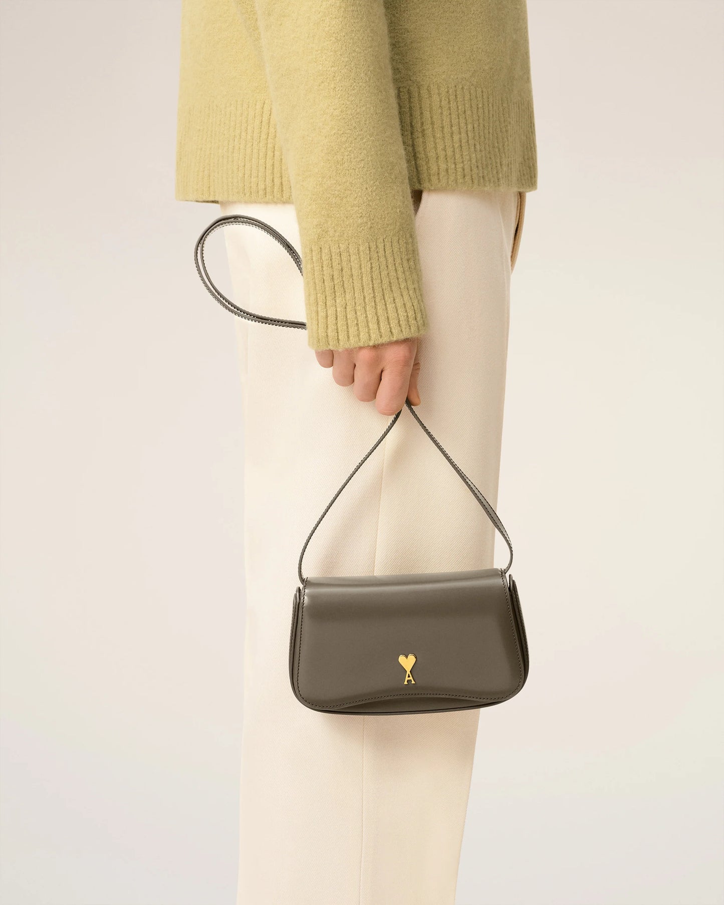Green handbag with a gold heart emblem on a light beige background ami paris