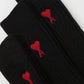 Black sock with a red heart design and 'ami' label on a light gray background