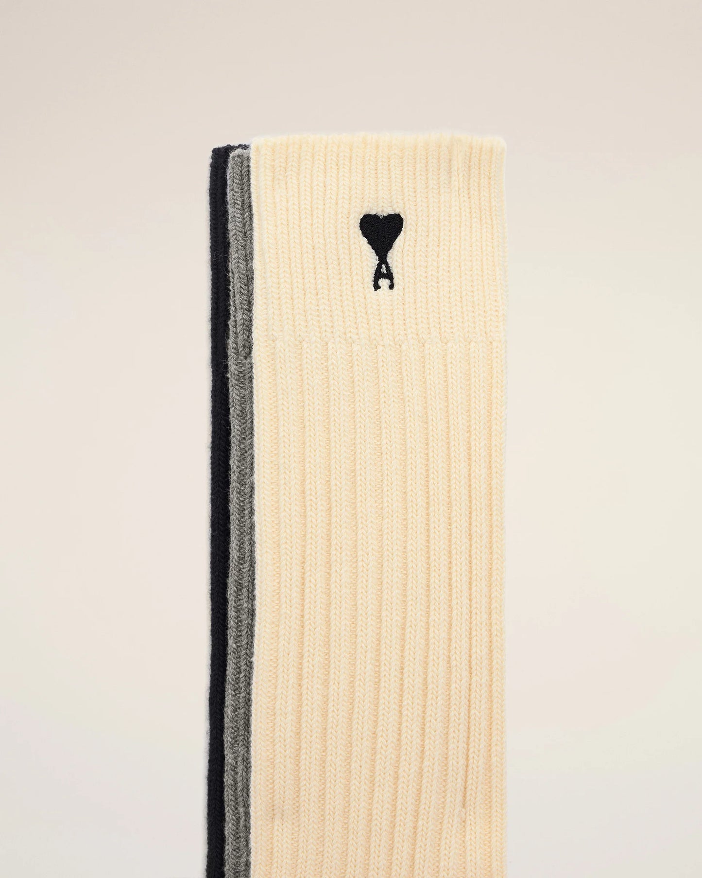 Three pairs of socks in beige, gray, and black on a light beige background