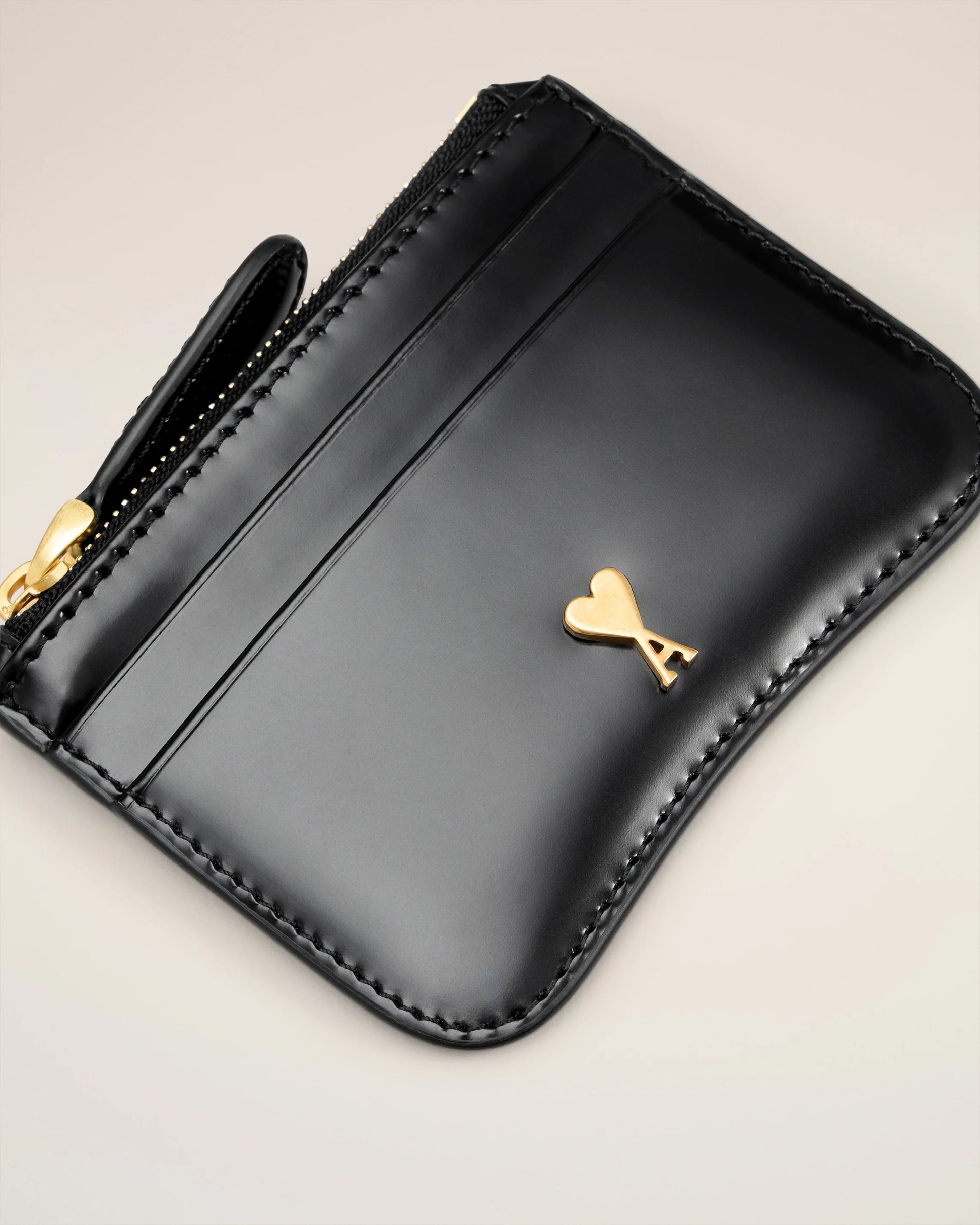Black wallet with gold heart emblem on a beige background