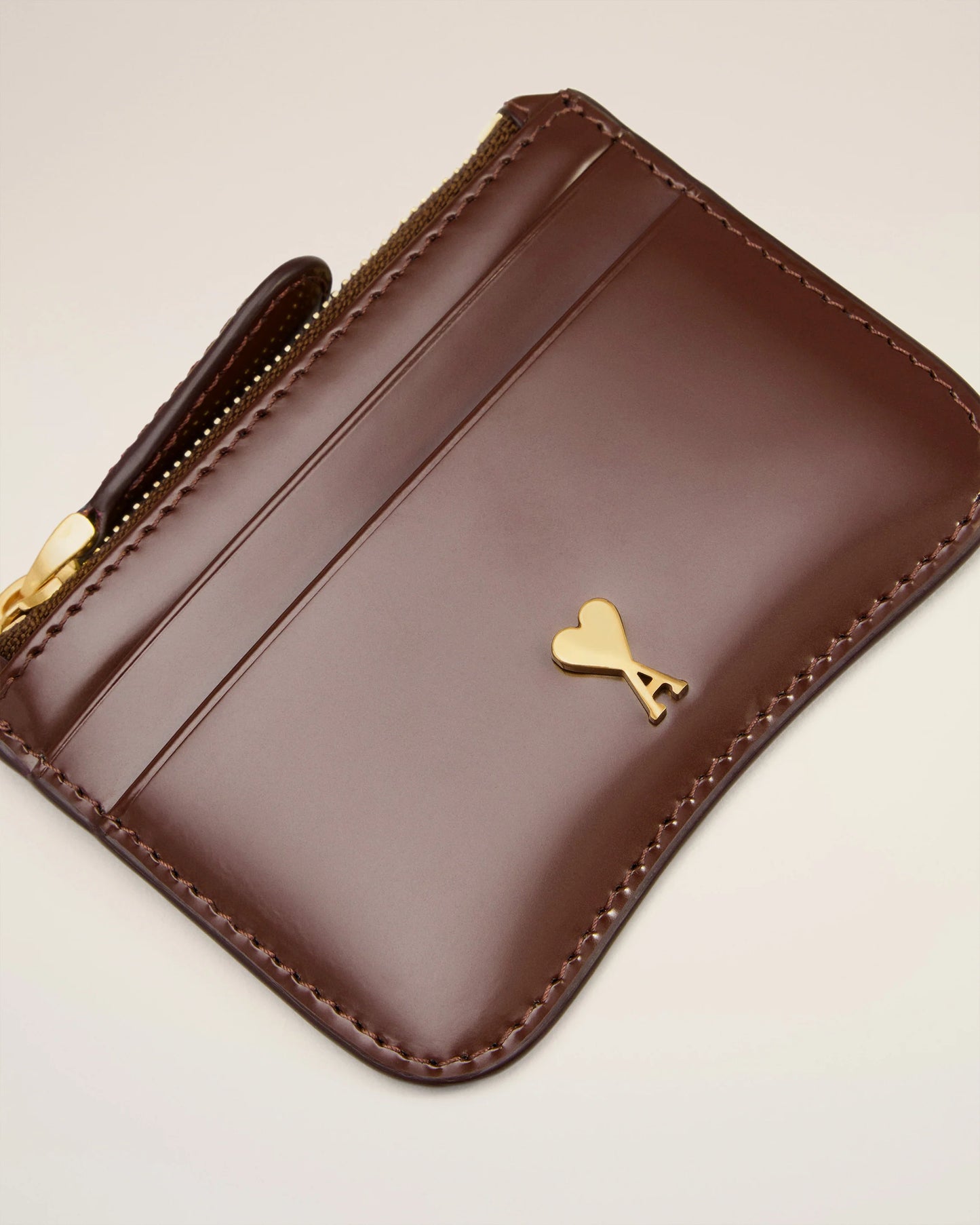 Brown leather wallet with gold zipper and heart emblem on a beige background
