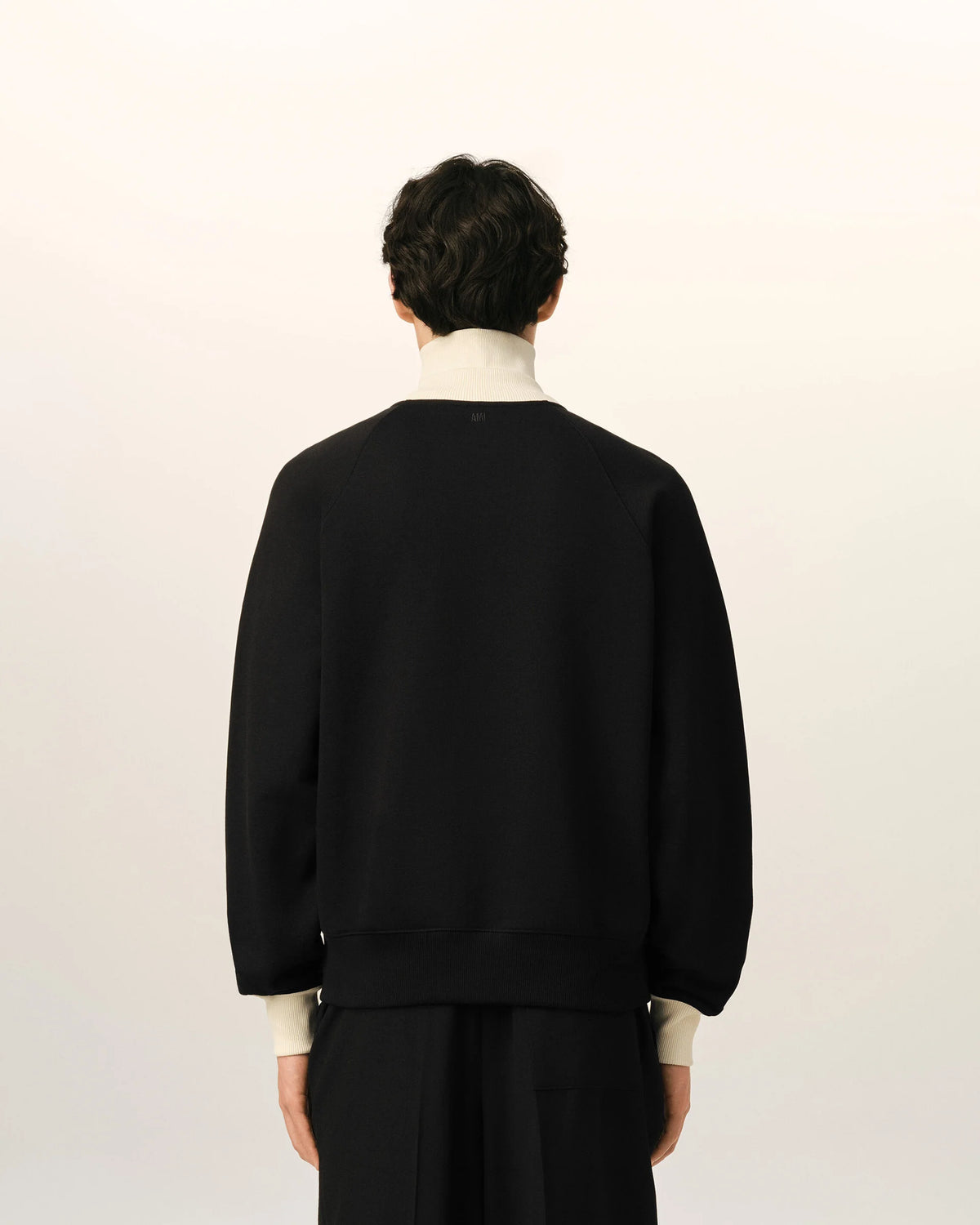 A black zip-up jacket with cream ribbed collar, cuffs, and hem, featuring a small embroidered logo on the left chest, displayed on a mannequin against a light beige background.