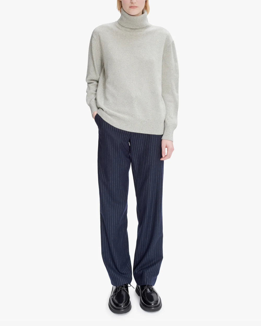 Person wearing a light gray turtleneck sweater and dark pinstripe pants on a white background