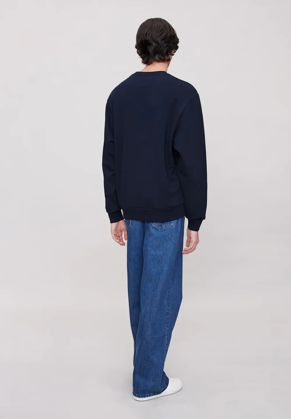 Person wearing a navy blue sweatshirt and blue jeans on a plain background