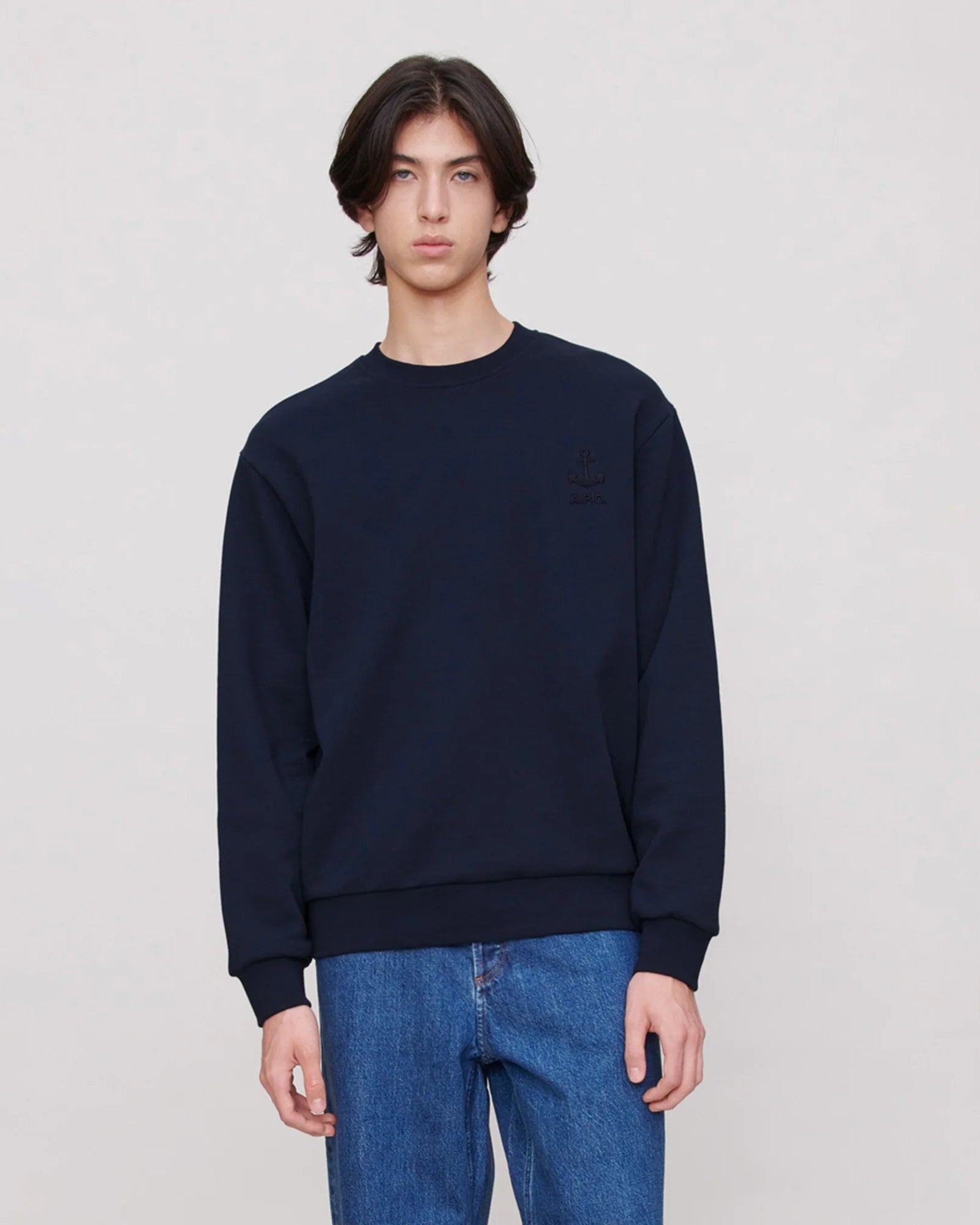 Person wearing a navy blue sweatshirt and blue jeans on a plain background
