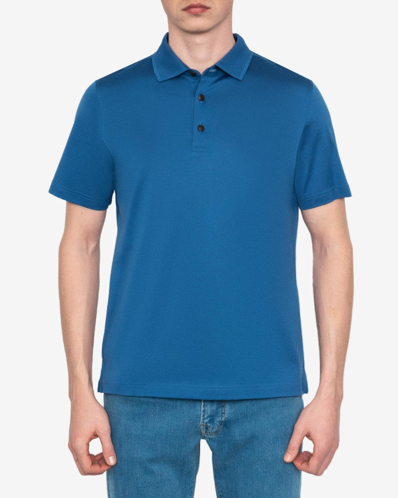 Person wearing a blue polo shirt and jeans on a plain background