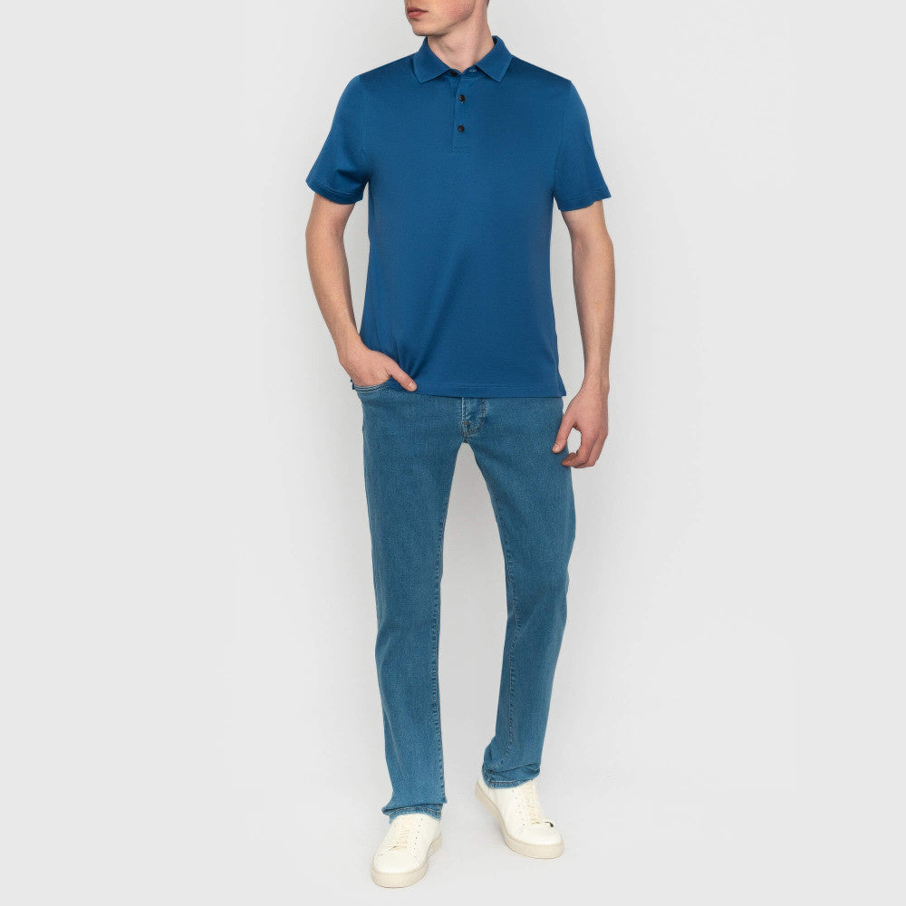 Person wearing a blue polo shirt and jeans on a plain background
