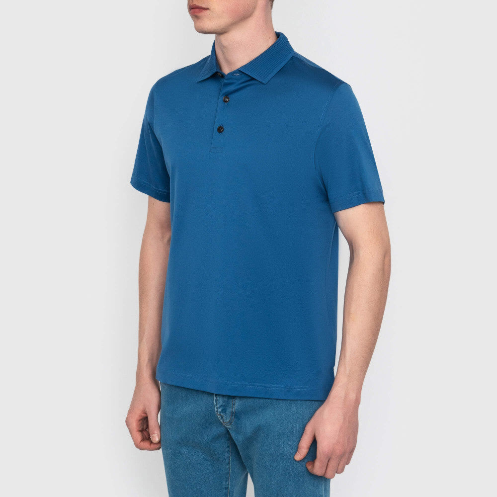 Person wearing a blue polo shirt and jeans on a plain background