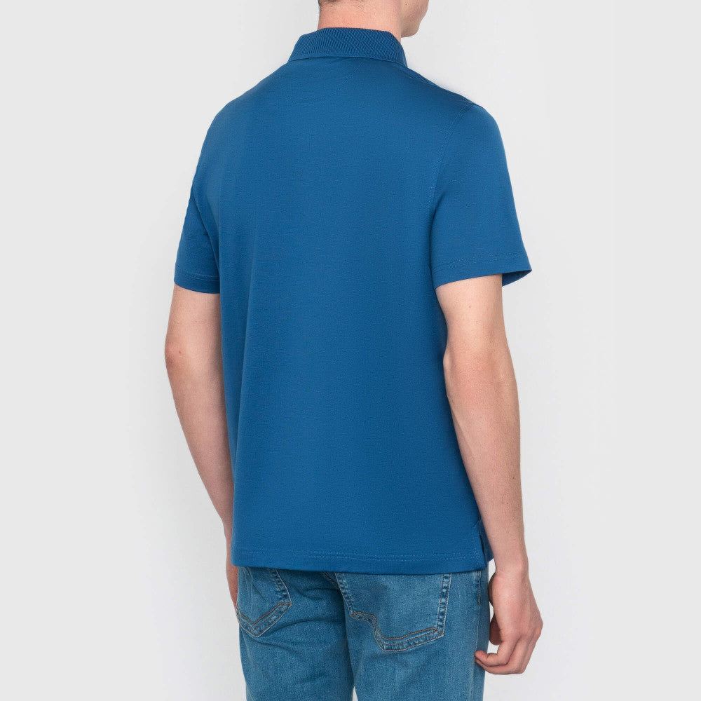 Person wearing a blue polo shirt and jeans on a plain background