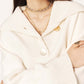 Woman wearing a cream-colored sweater and multiple necklaces on a white background
