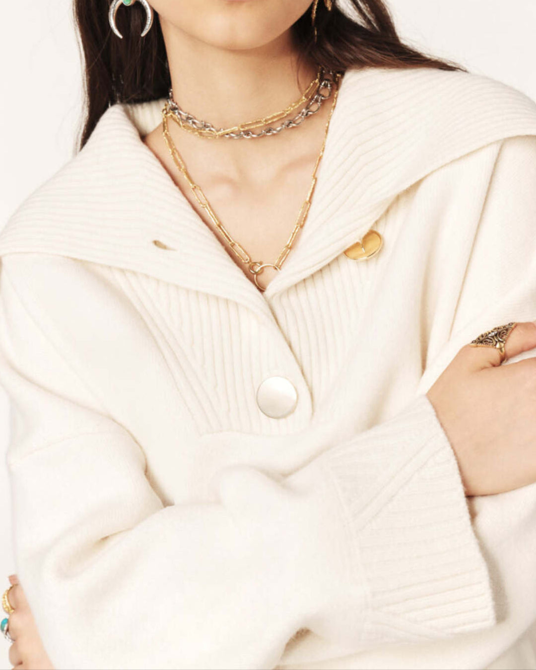 Woman wearing a cream-colored sweater and multiple necklaces on a white background