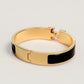 Gold bracelet with black band on a light gray background