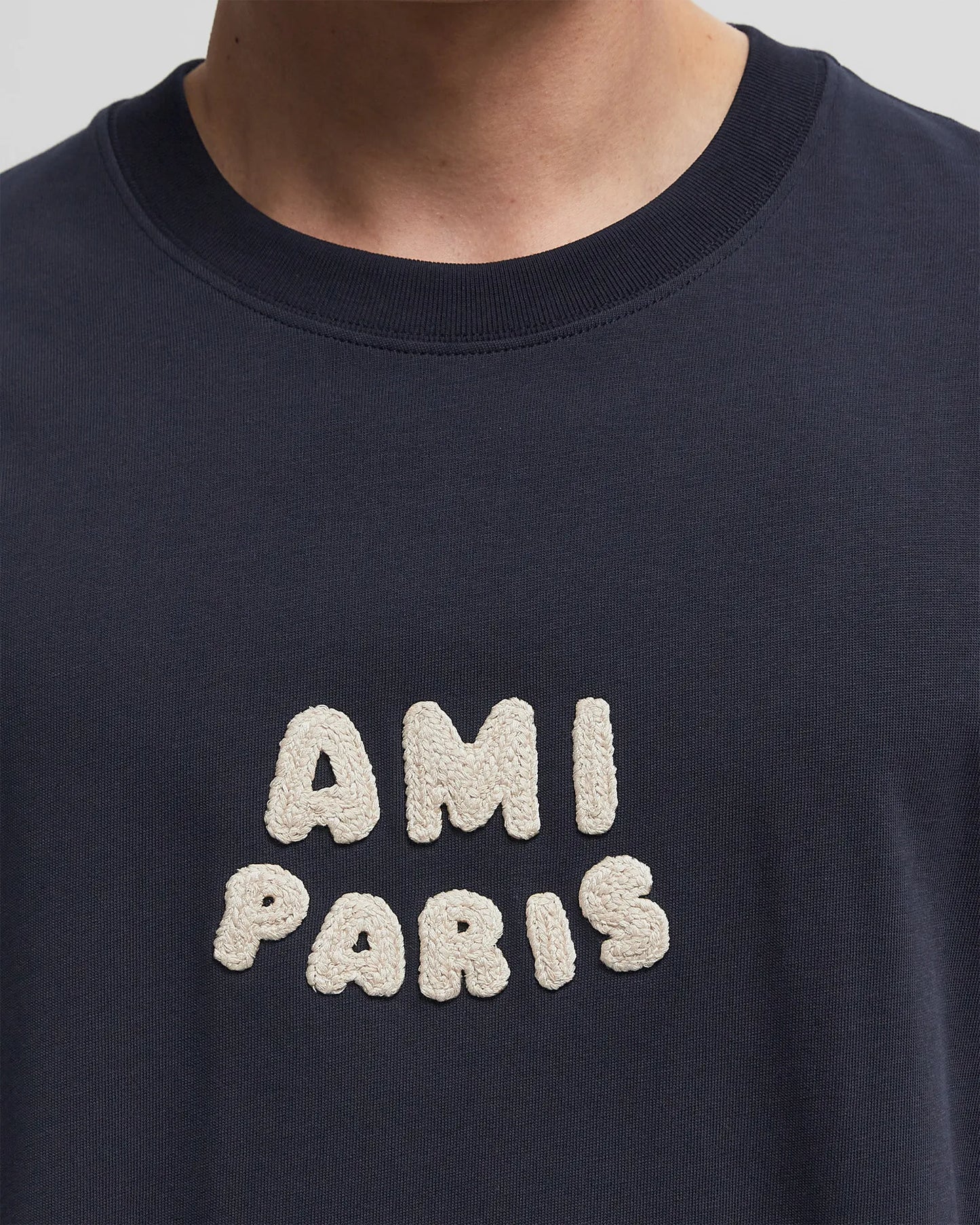 Navy blue t-shirt with 'AMI PARIS' text on a light gray background