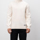 Man wearing a white turtleneck sweater with a logo on a plain background
