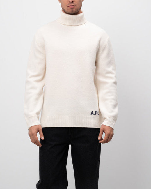 Man wearing a white turtleneck sweater with a logo on a plain background