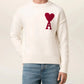 Person wearing a white sweater with a red heart and letter 'A' design, paired with blue jeans on a light background.