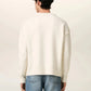Person wearing a white sweater with a red heart and letter 'A' design, paired with blue jeans on a light background.