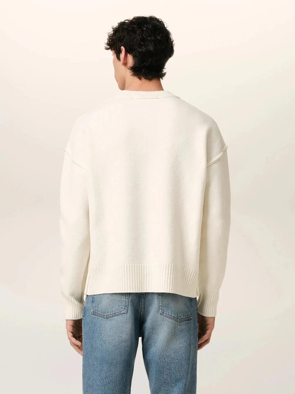 Person wearing a white sweater with a red heart and letter 'A' design, paired with blue jeans on a light background.