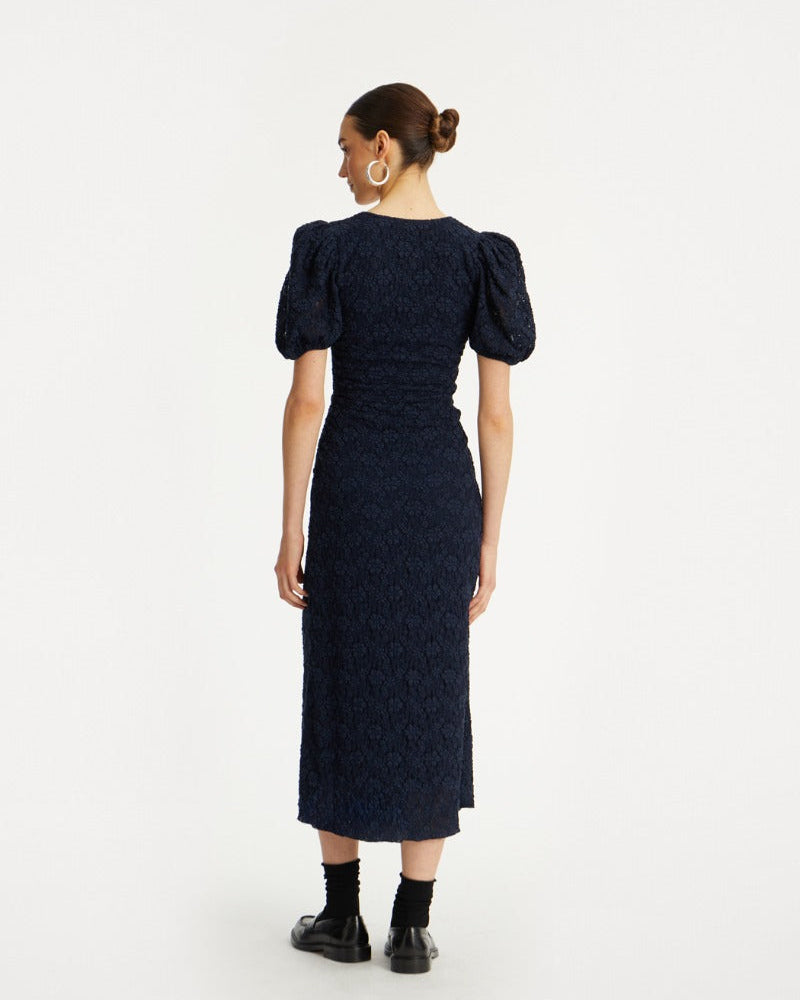 Woman wearing a dark blue dress with puff sleeves on a white background